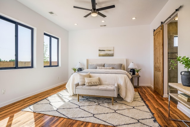 bedroom with a barn door, ceiling fan, and dark hardwood / wood-style flooring