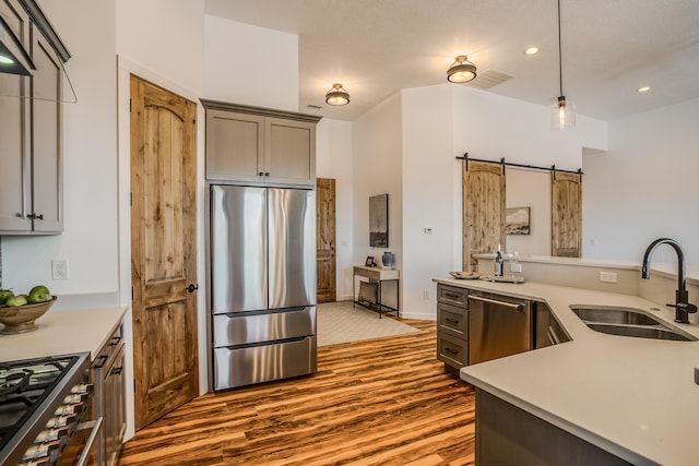 kitchen with hanging light fixtures, stainless steel appliances, sink, hardwood / wood-style flooring, and a barn door