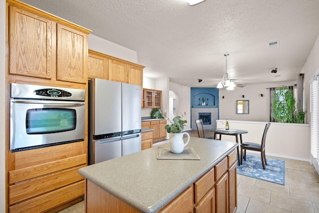 kitchen featuring ceiling fan, appliances with stainless steel finishes, a textured ceiling, a fireplace, and a center island