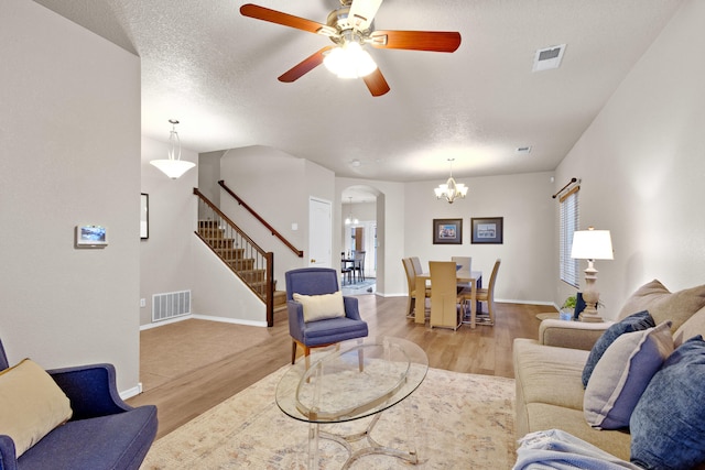 living room featuring light hardwood / wood-style flooring, a textured ceiling, and ceiling fan with notable chandelier