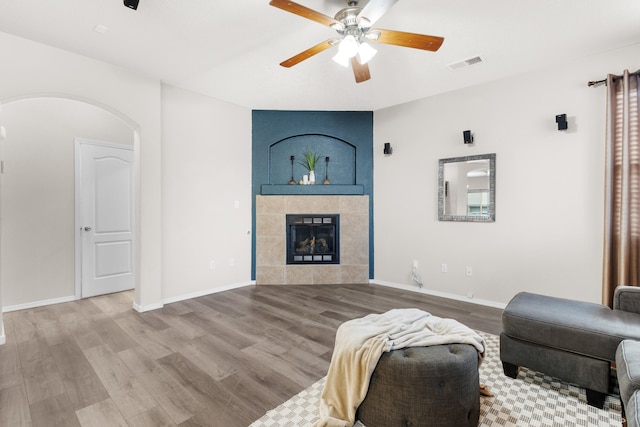 living room featuring a tiled fireplace, wood-type flooring, and ceiling fan