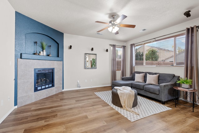 living room featuring a textured ceiling, hardwood / wood-style flooring, a fireplace, and ceiling fan