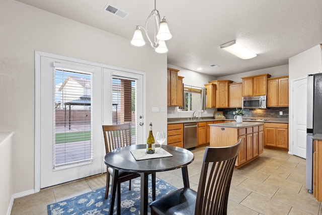 kitchen with a kitchen island, sink, a notable chandelier, pendant lighting, and appliances with stainless steel finishes