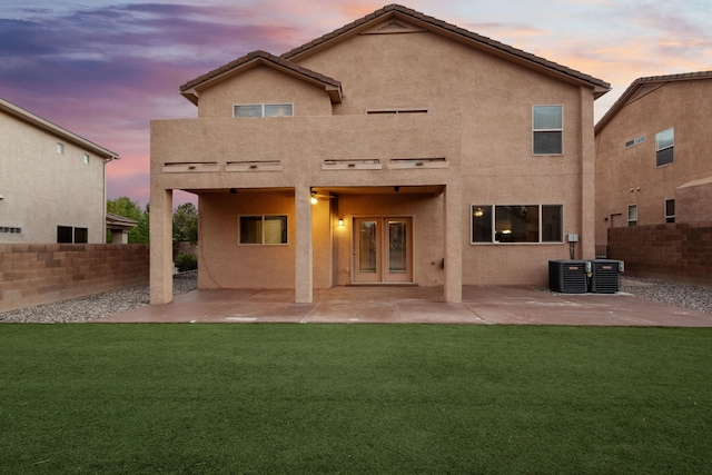 back house at dusk with a patio, central AC, and a lawn