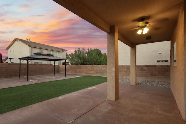 patio terrace at dusk with a gazebo, a lawn, and ceiling fan