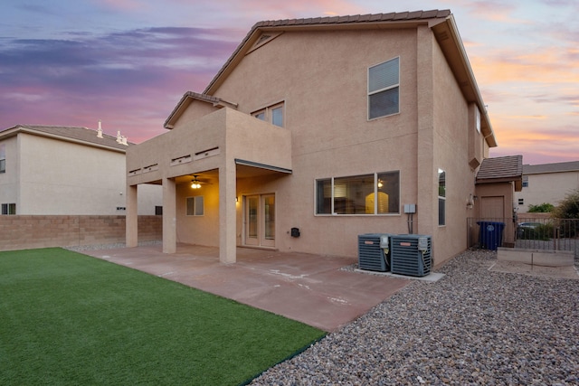 back house at dusk featuring a patio area, a lawn, a balcony, and central AC unit