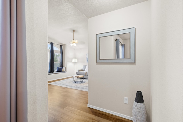 corridor featuring a textured ceiling, a chandelier, and light wood-type flooring