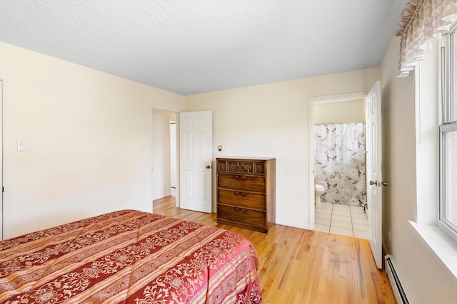 bedroom featuring a baseboard heating unit, connected bathroom, a textured ceiling, and light wood-type flooring