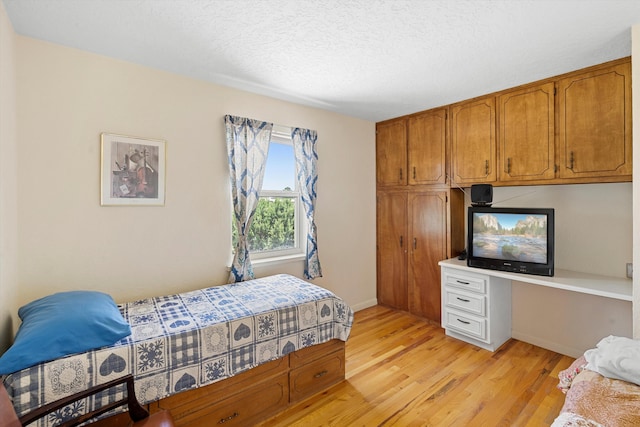 bedroom featuring a textured ceiling, built in desk, and light hardwood / wood-style floors