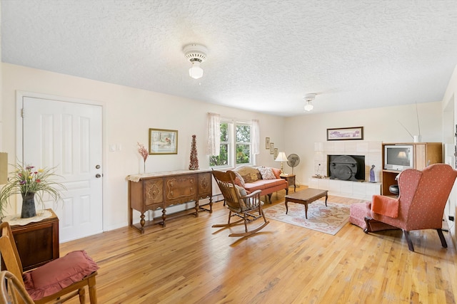 living room with a textured ceiling, light hardwood / wood-style flooring, a baseboard radiator, and a tile fireplace