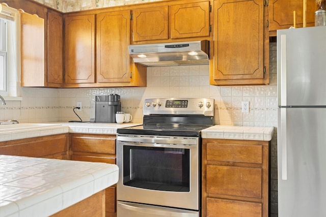 kitchen featuring decorative backsplash, tile counters, appliances with stainless steel finishes, and sink