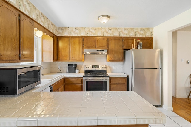 kitchen featuring light hardwood / wood-style floors, appliances with stainless steel finishes, tile countertops, and kitchen peninsula