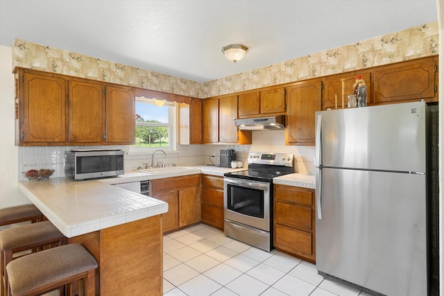 kitchen with kitchen peninsula, appliances with stainless steel finishes, light tile patterned floors, and sink