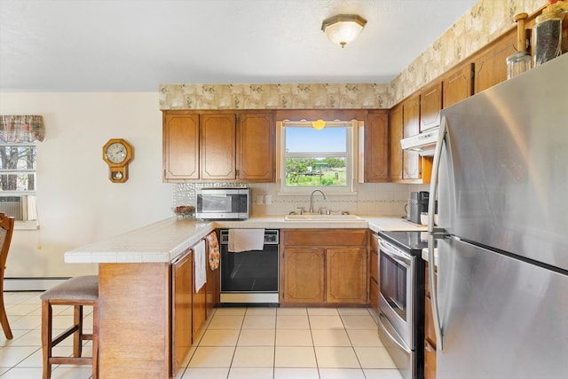 kitchen featuring a breakfast bar, sink, kitchen peninsula, a baseboard radiator, and appliances with stainless steel finishes