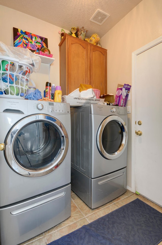 laundry area featuring cabinets, a textured ceiling, light tile patterned floors, and washing machine and clothes dryer