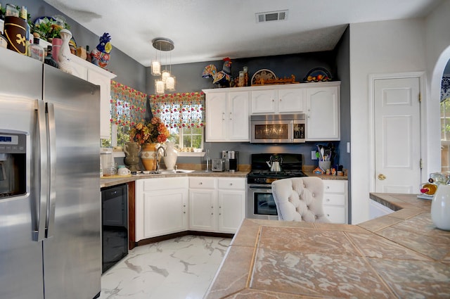 kitchen featuring decorative light fixtures, appliances with stainless steel finishes, tile counters, and white cabinetry