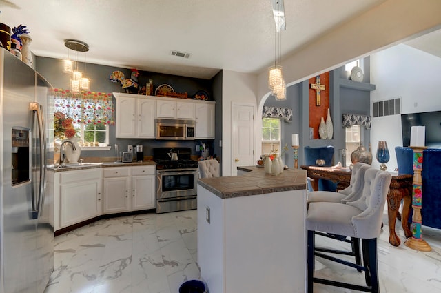 kitchen with white cabinets, pendant lighting, sink, stainless steel appliances, and a breakfast bar