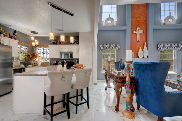 kitchen with white cabinets, a textured ceiling, decorative light fixtures, appliances with stainless steel finishes, and a breakfast bar