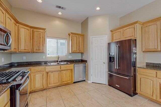 kitchen with light brown cabinets, light tile patterned flooring, sink, appliances with stainless steel finishes, and dark stone countertops