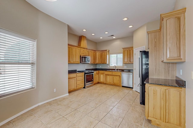 kitchen with appliances with stainless steel finishes, dark stone countertops, light tile patterned flooring, and sink