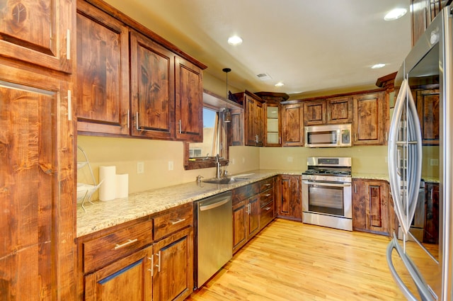 kitchen with light stone counters, sink, light hardwood / wood-style flooring, appliances with stainless steel finishes, and decorative light fixtures