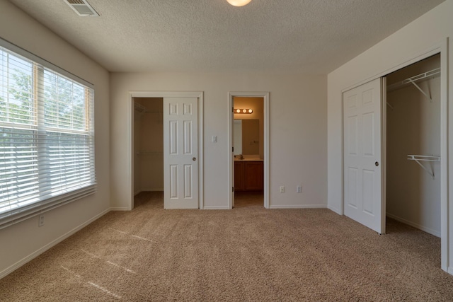 unfurnished bedroom with ensuite bath, light colored carpet, a textured ceiling, and multiple windows