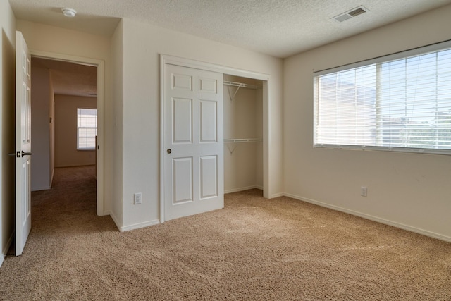 unfurnished bedroom featuring light carpet, a closet, multiple windows, and a textured ceiling