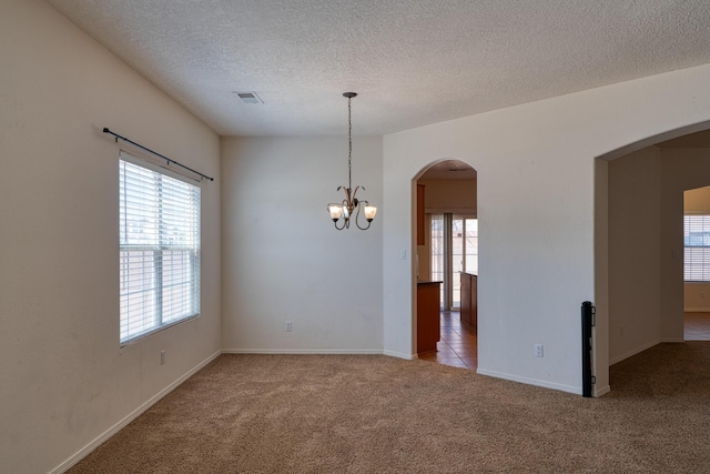 carpeted spare room featuring a textured ceiling, an inviting chandelier, and plenty of natural light