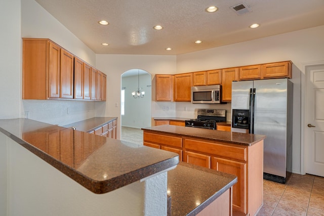 kitchen with dark stone countertops, a chandelier, stainless steel appliances, a center island, and light tile patterned flooring