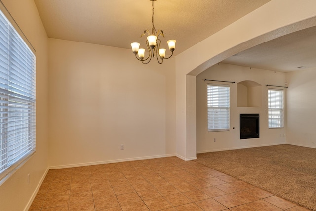 unfurnished living room featuring an inviting chandelier, light tile patterned floors, and a textured ceiling