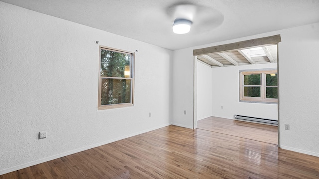 empty room featuring ceiling fan, a baseboard heating unit, a skylight, and hardwood / wood-style flooring