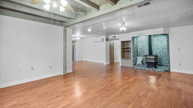 unfurnished living room featuring track lighting, a wood stove, beam ceiling, light hardwood / wood-style flooring, and ceiling fan