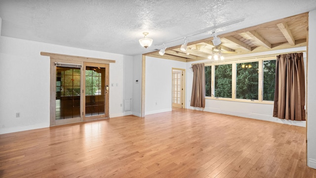 empty room featuring light wood-type flooring, a textured ceiling, beam ceiling, ceiling fan, and track lighting