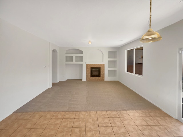 unfurnished living room with built in shelves, light carpet, and a tile fireplace