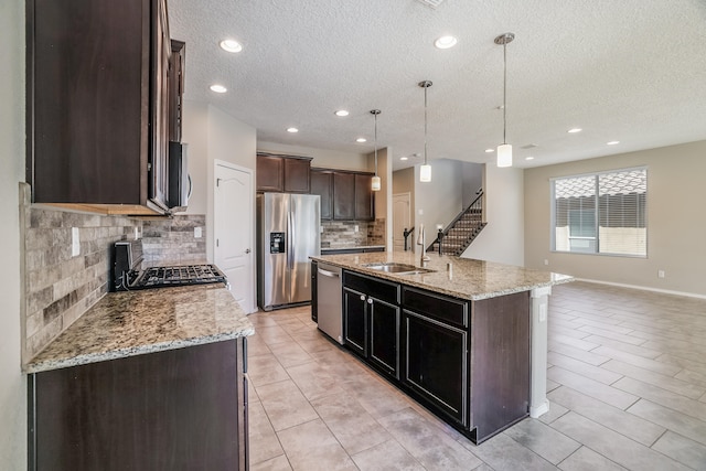 kitchen featuring hanging light fixtures, sink, a textured ceiling, a kitchen island with sink, and stainless steel appliances