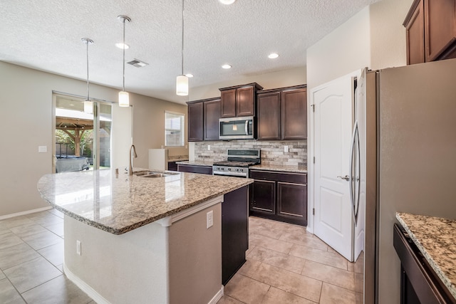 kitchen featuring light stone counters, stainless steel appliances, a textured ceiling, a center island with sink, and sink