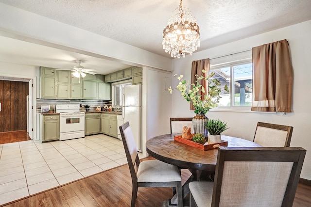 dining space featuring ceiling fan with notable chandelier, a textured ceiling, and light hardwood / wood-style flooring