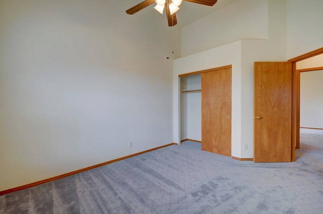 unfurnished bedroom with a high ceiling, light colored carpet, a closet, and ceiling fan