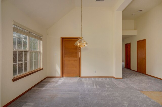 carpeted spare room featuring high vaulted ceiling and a chandelier