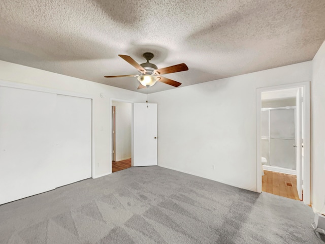 unfurnished bedroom with ensuite bath, a textured ceiling, ceiling fan, carpet floors, and a closet