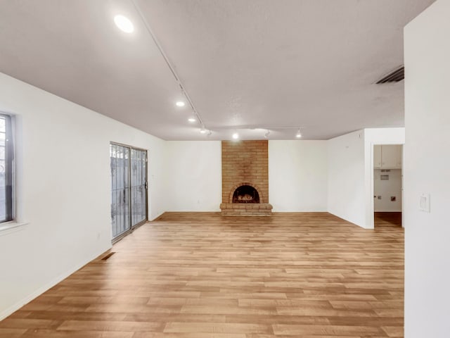 unfurnished living room with track lighting, a fireplace, and light hardwood / wood-style flooring