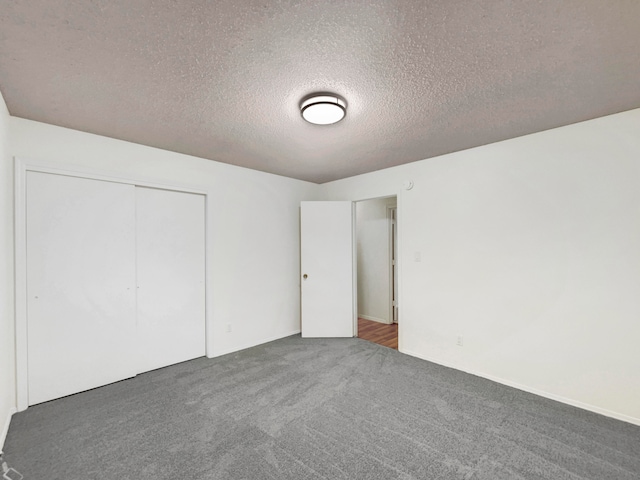 unfurnished bedroom with dark carpet, a textured ceiling, and a closet