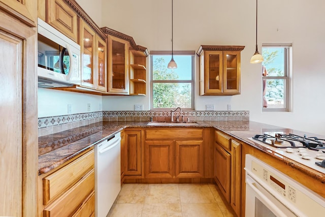 kitchen featuring decorative light fixtures, dark stone countertops, white appliances, and sink