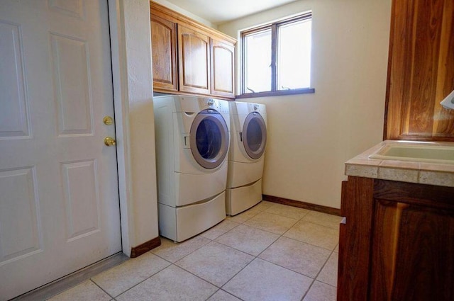 laundry room with cabinets, light tile patterned floors, separate washer and dryer, and sink