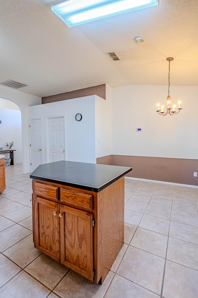 kitchen with a kitchen island, light tile patterned floors, pendant lighting, a textured ceiling, and an inviting chandelier