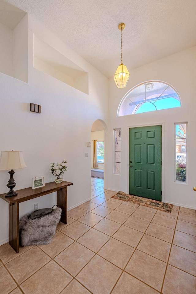 foyer entrance featuring a towering ceiling, a textured ceiling, plenty of natural light, and light tile patterned floors