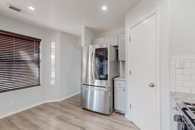 kitchen with white cabinets, stove, decorative backsplash, light stone countertops, and stainless steel fridge