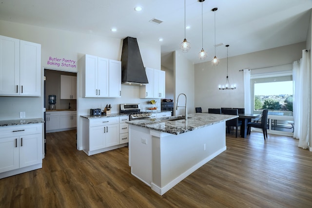 kitchen with gas range, wall chimney exhaust hood, white cabinetry, and a kitchen island with sink