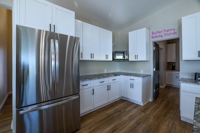 kitchen featuring dark wood-type flooring, white cabinetry, appliances with stainless steel finishes, dark stone counters, and vaulted ceiling