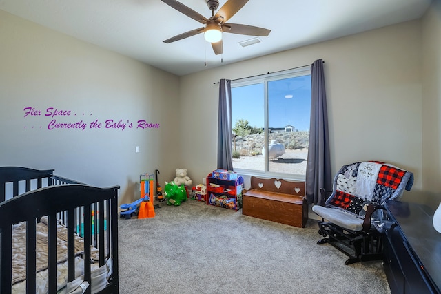 carpeted bedroom featuring a crib and ceiling fan